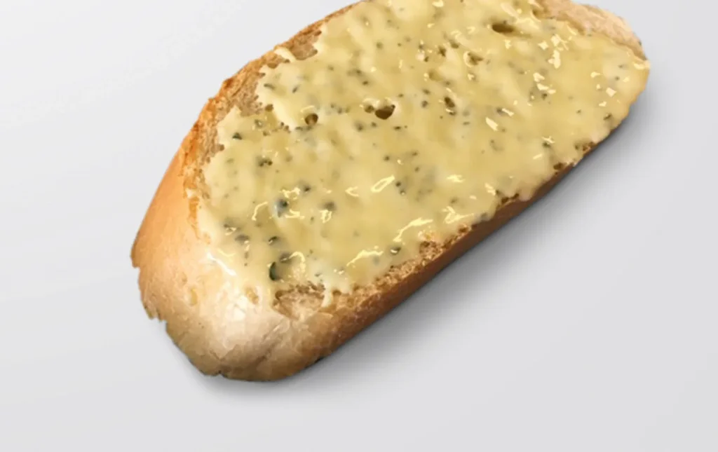 Slice of bread with a layer of garlic butter with herbs, on a light grey background