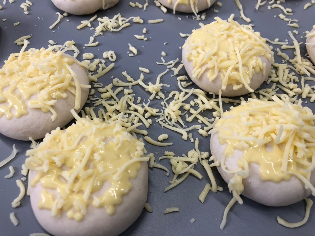 Dough balls with cheese sauce and grated cheese on a grey baking tray