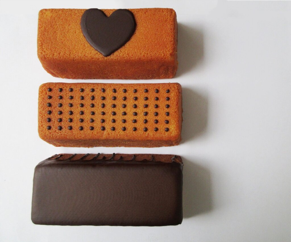 Three loaf cakes seen from above: one with a chocolate heart, one with a chocolate dot grid, one fully covered in chocolate