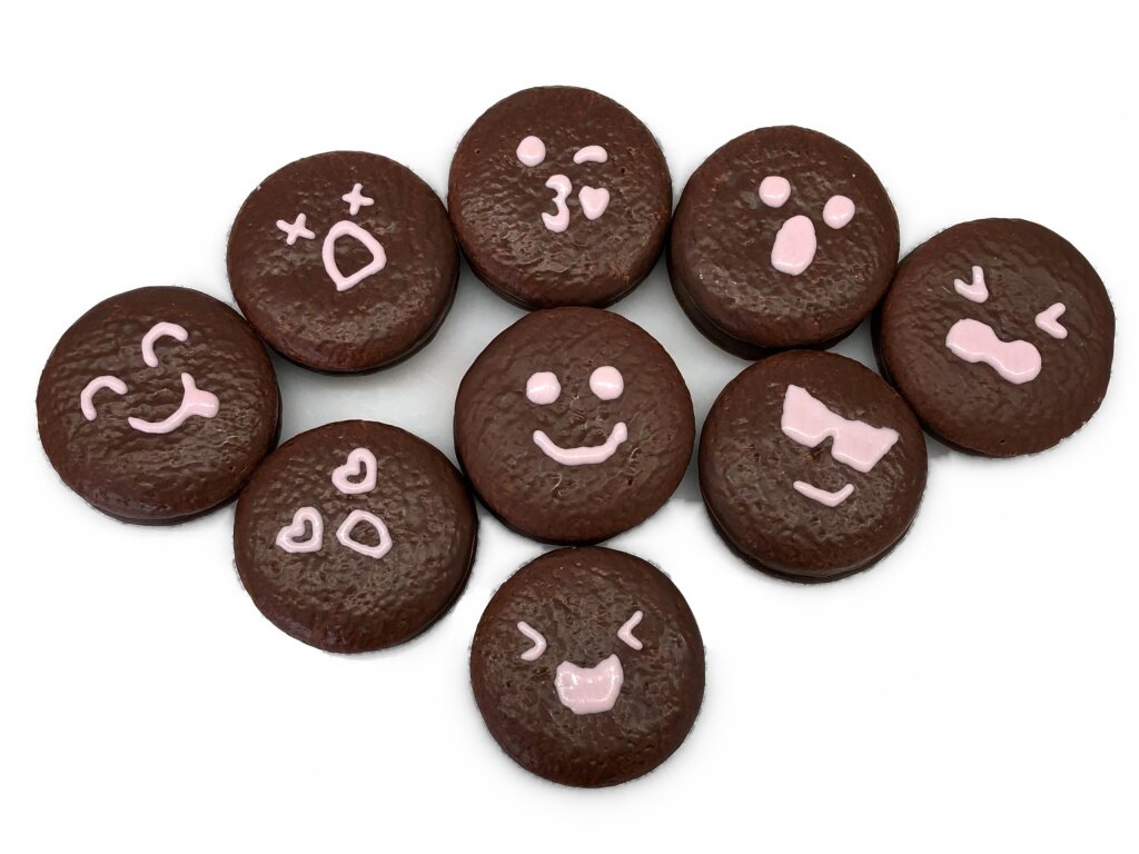 Nine chocolate coated cakes, each with a different small face deposited in pink
