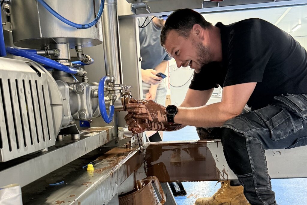 FoodJet engineer under a depositor, laughing, with his hands covered in chocolate